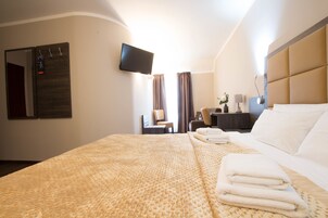 Ein Hotelzimmer mit einem großen Bett, einem flachbildfernseher an der Wand, einem Schreibtisch mit Lampe und einem Sessel.