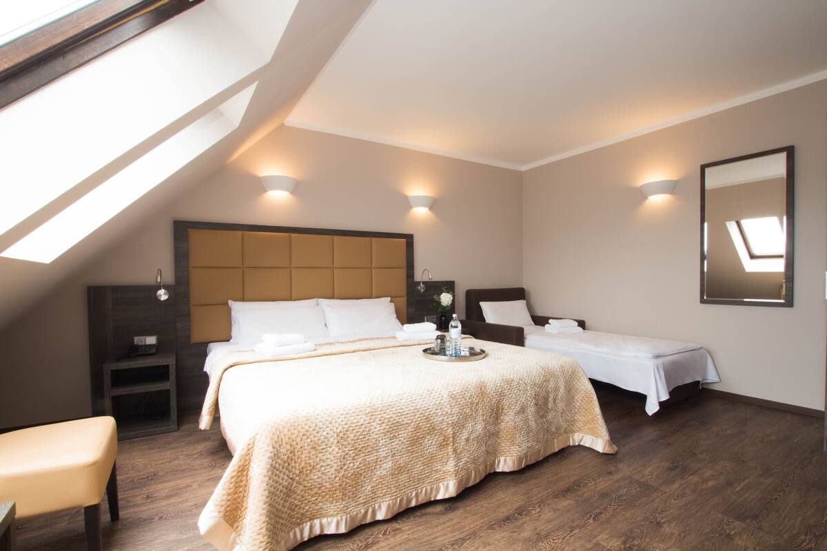 Un dormitorio con una cama grande, dos mesitas de noche, un banco y un tragaluz.