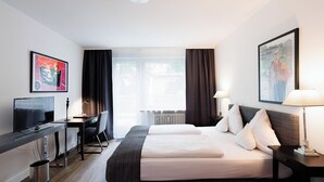 Une chambre d’hôtel avec un lit, un bureau avec un ordinateur, une télévision et deux tableaux accrochés aux murs.