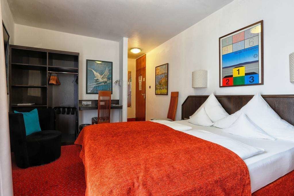 A hotel room with a large bed, a desk, a chair, and a bookshelf.