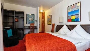 A hotel room with a large bed, a desk, a chair, and a bookshelf.