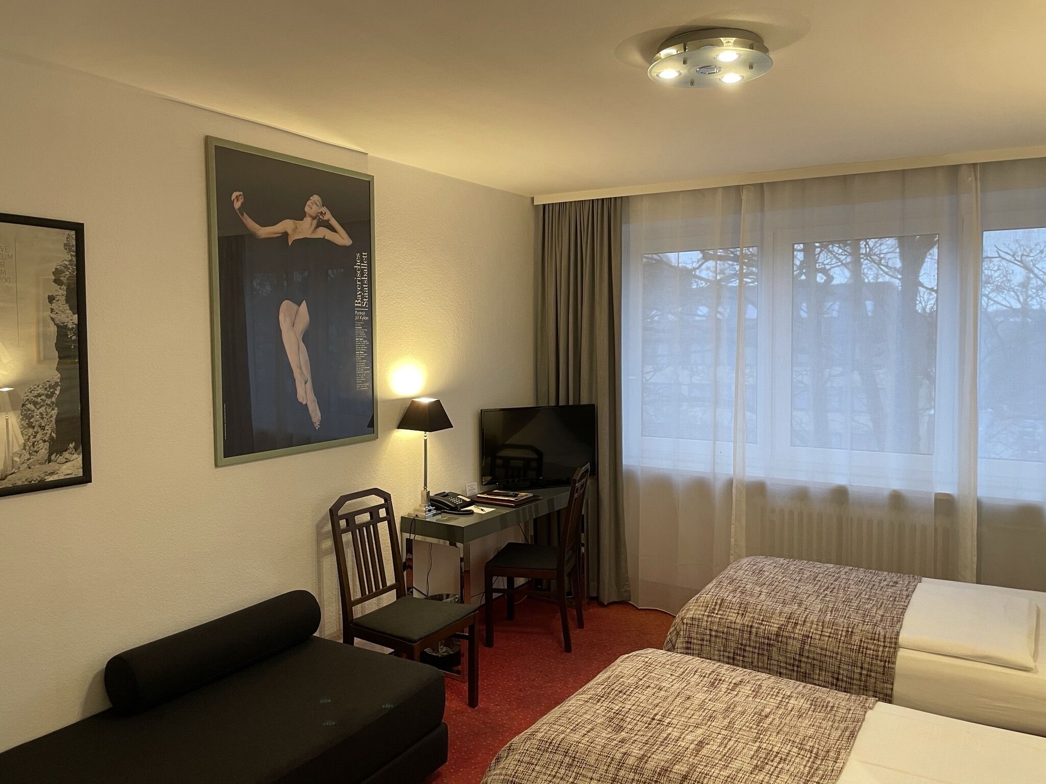 Una habitación de hotel con cama, escritorio, computadora, sillón y televisor.