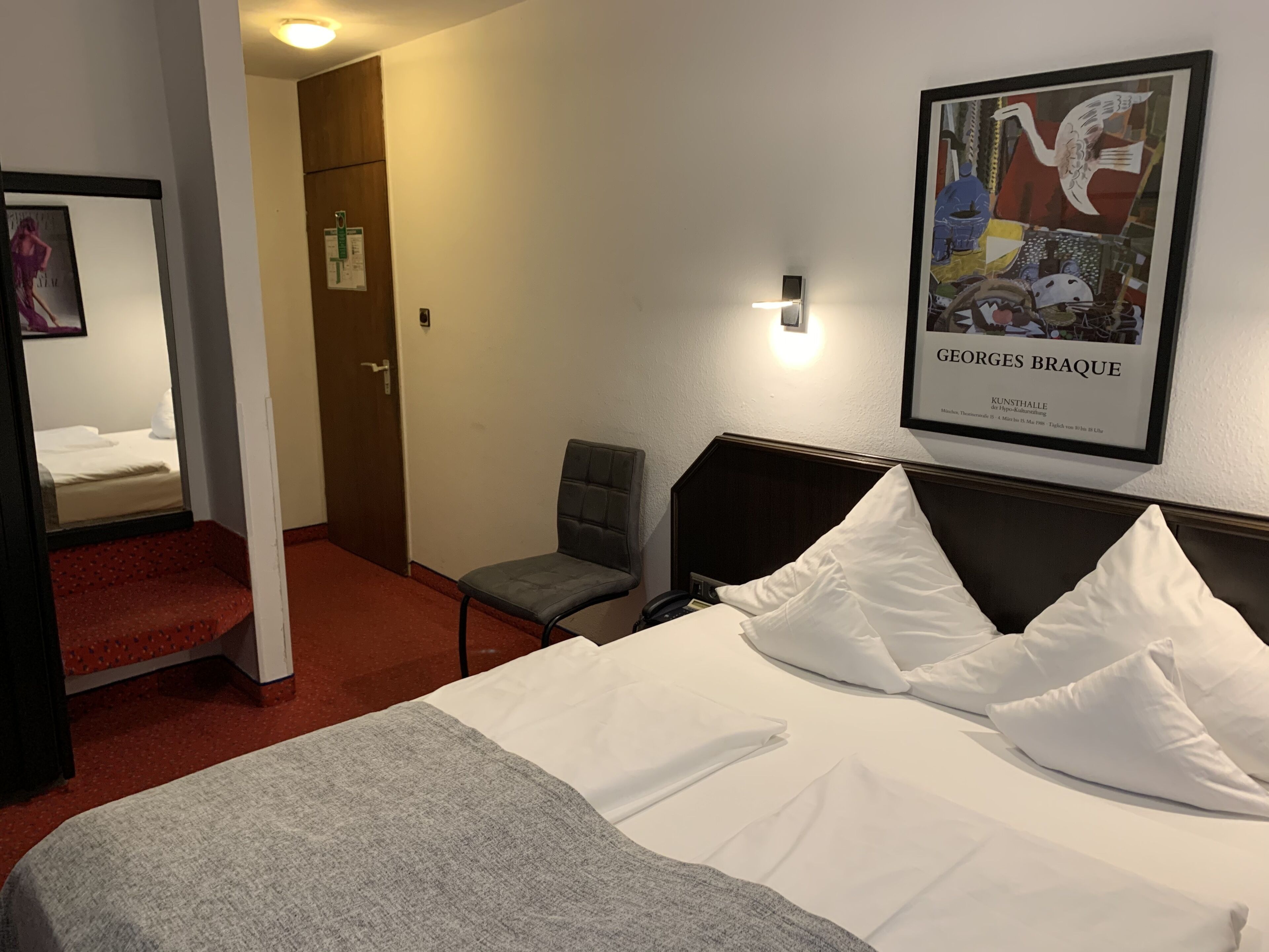 Habitación de hotel con una cama, una silla, un escritorio y un cuadro en la pared.