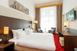 A hotel room with a large bed, two bedside tables, a desk, a chair, and a TV. - Leonardo Hotel Berlin KU'DAMM (Berlin)