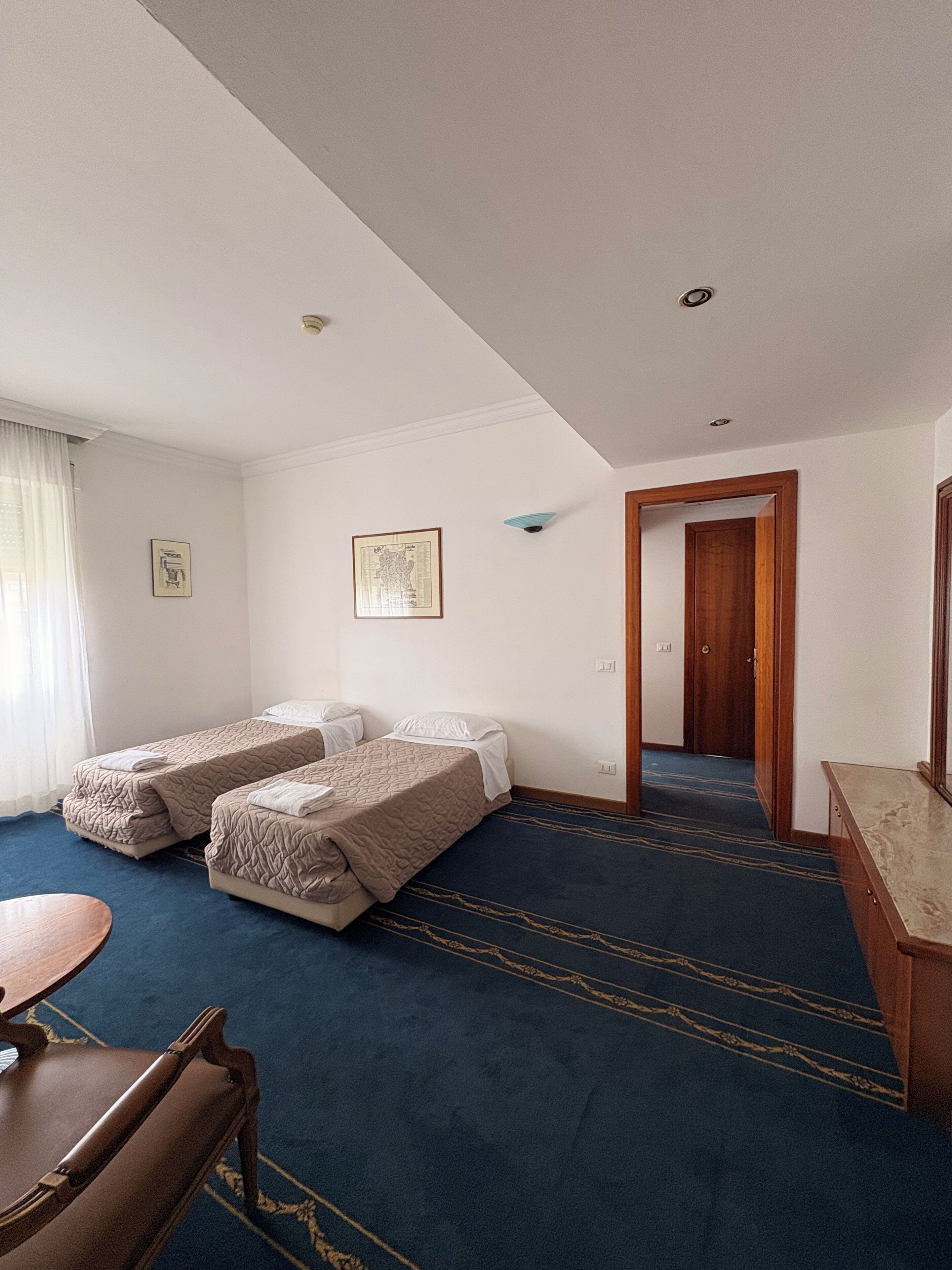 Ein Hotelzimmer mit zwei Betten, einem Schreibtisch, einem Stuhl, einer Tür und einem kleinen Tisch.