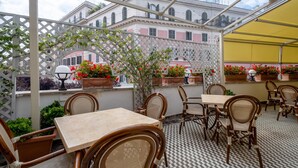 Un café al aire libre con mesas y sillas, una estructura de celosía y plantas en macetas.