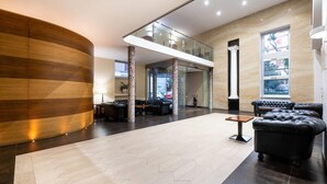 Un vestíbulo espacioso con un mostrador de recepción de madera curvo, un sofá de cuero negro y un suelo con estampado de espiga.