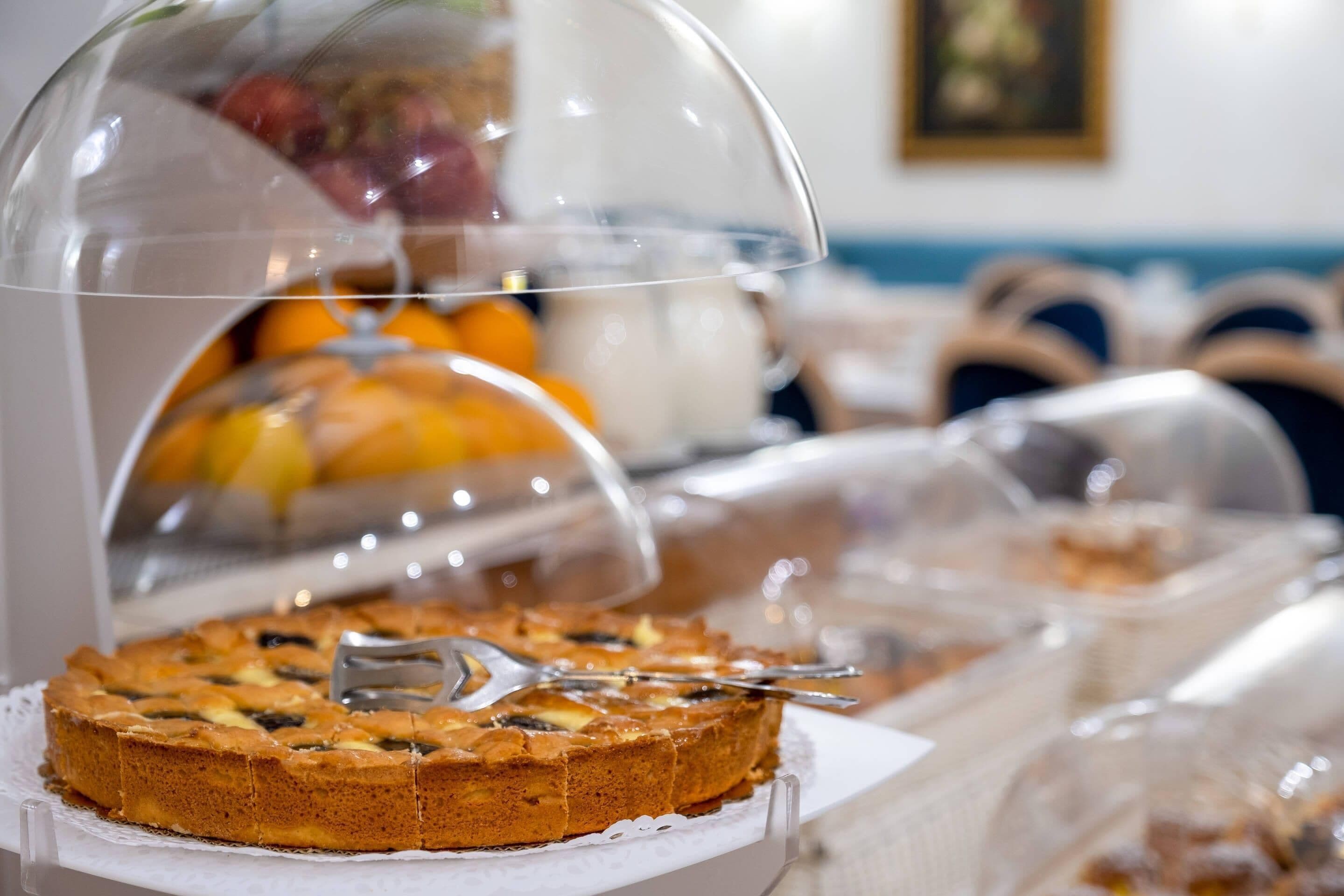 A dessert display with a covered cake and fruits under a glass dome.