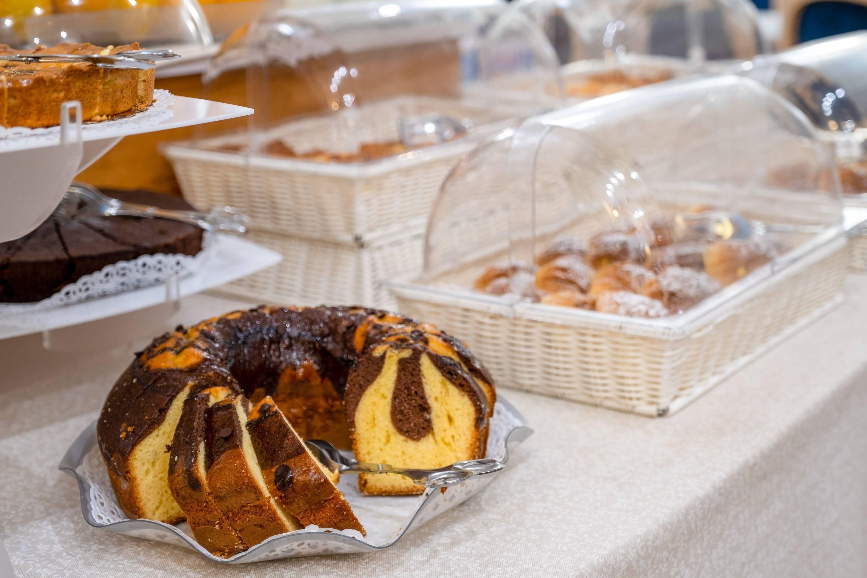 Un bufé con diversas opciones de panadería, incluyendo un pastel bundt y pasteles en cestas de mimbre.