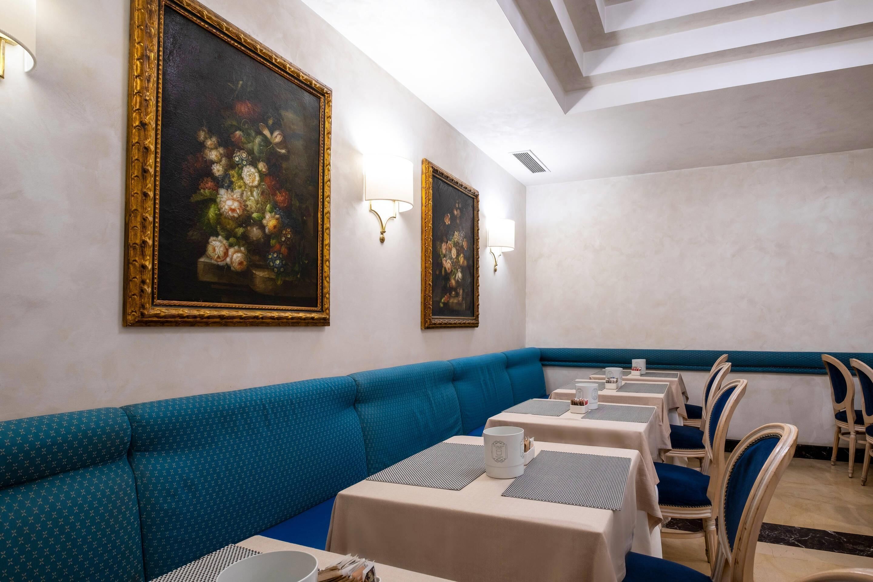A dining area with a blue cushioned bench, tables with white tablecloths, and wall-mounted light fixtures.