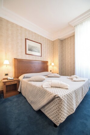 Habitación de hotel con una cama grande, dos lámparas de noche, cabecera de madera, un cuadro en la pared y una mesita de noche con teléfono.