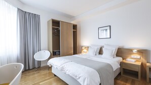 Ein modernes Hotelzimmer mit einem gro ßen Bett, Nachttischen, einem Kleiderschrank und einem kleinen weißen Stuhl.