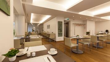 A modern hotel dining area with multiple tables and chairs, a wooden floor, and a clean, minimalist design.