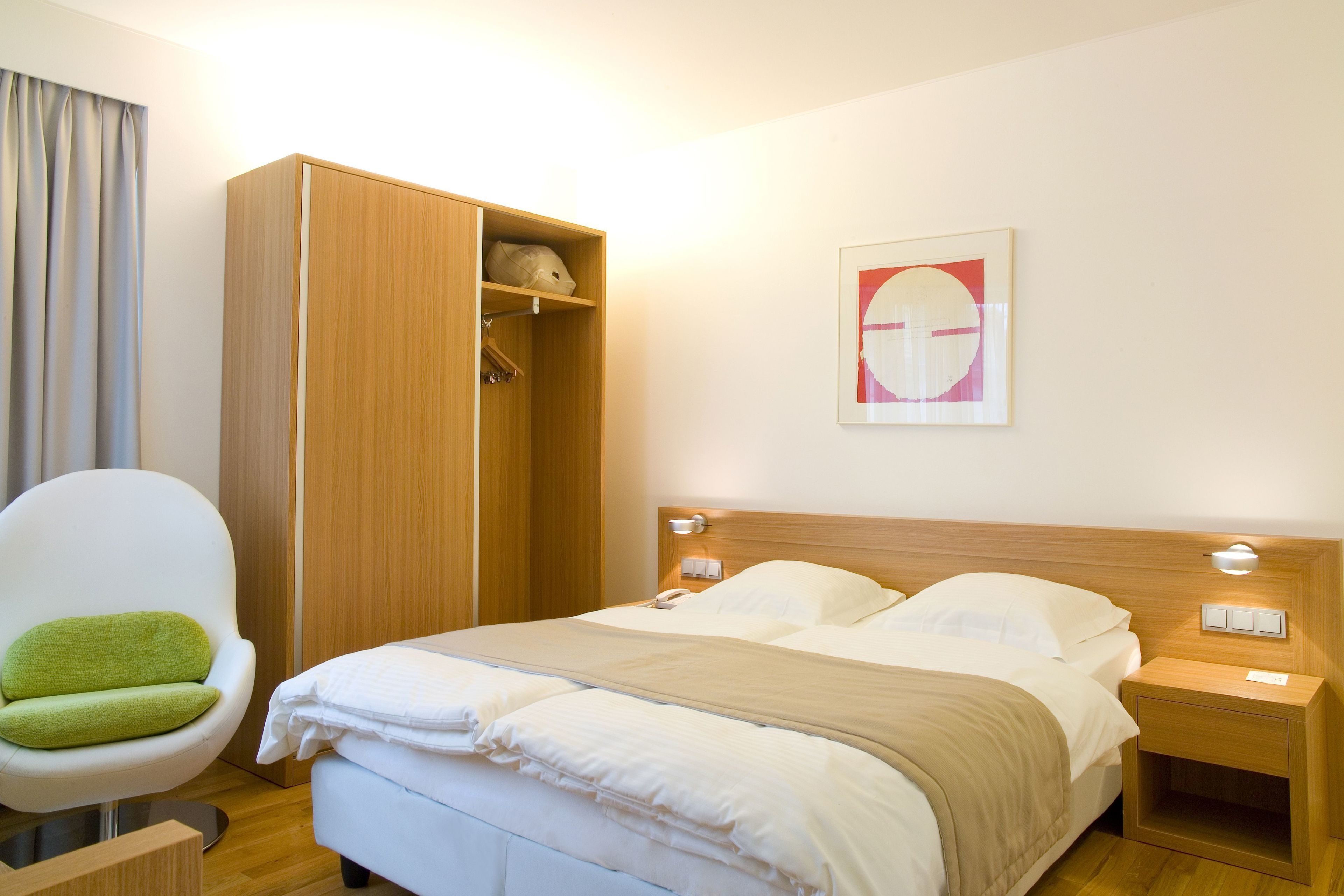 Een hotelkamer met een bed, een houten kledingkast, een stoel en een kunstwerk aan de muur.