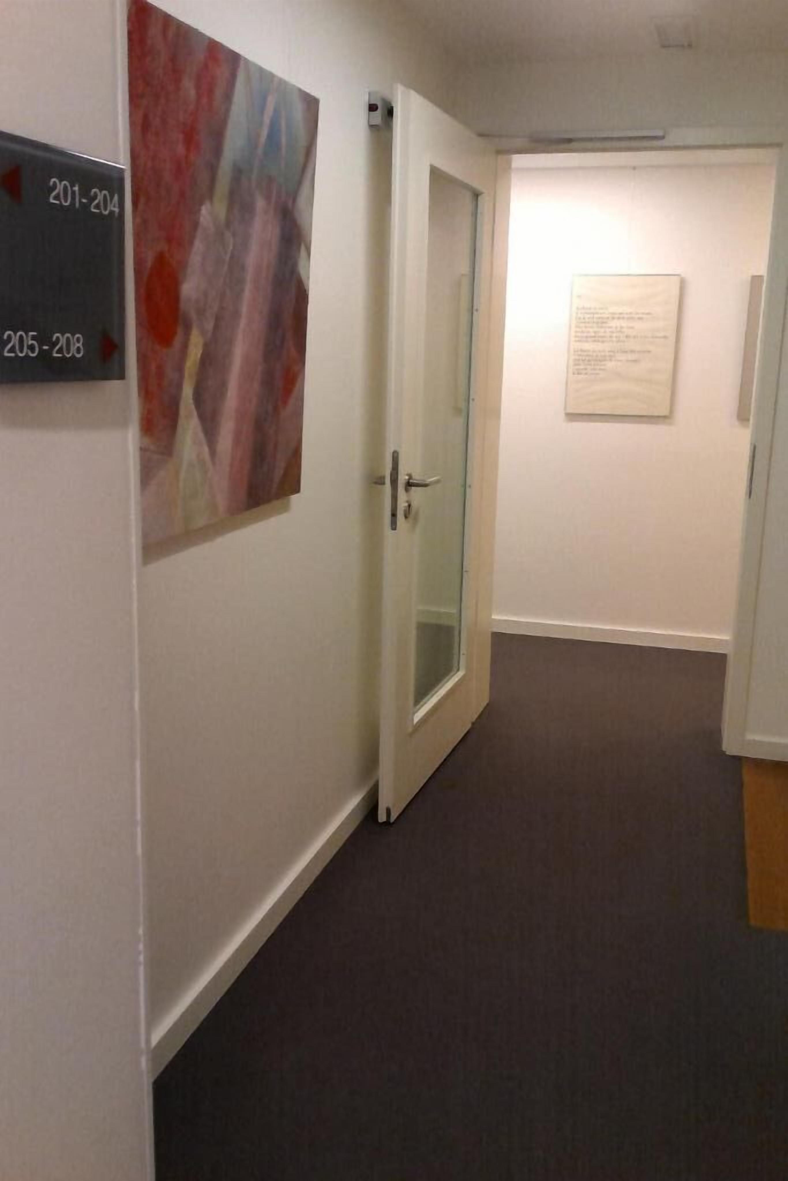Un pasillo con puerta de vidrio, un cartel que indica las habitaciones 201 a 204, y otro cartel para las habitaciones 205 a 208.