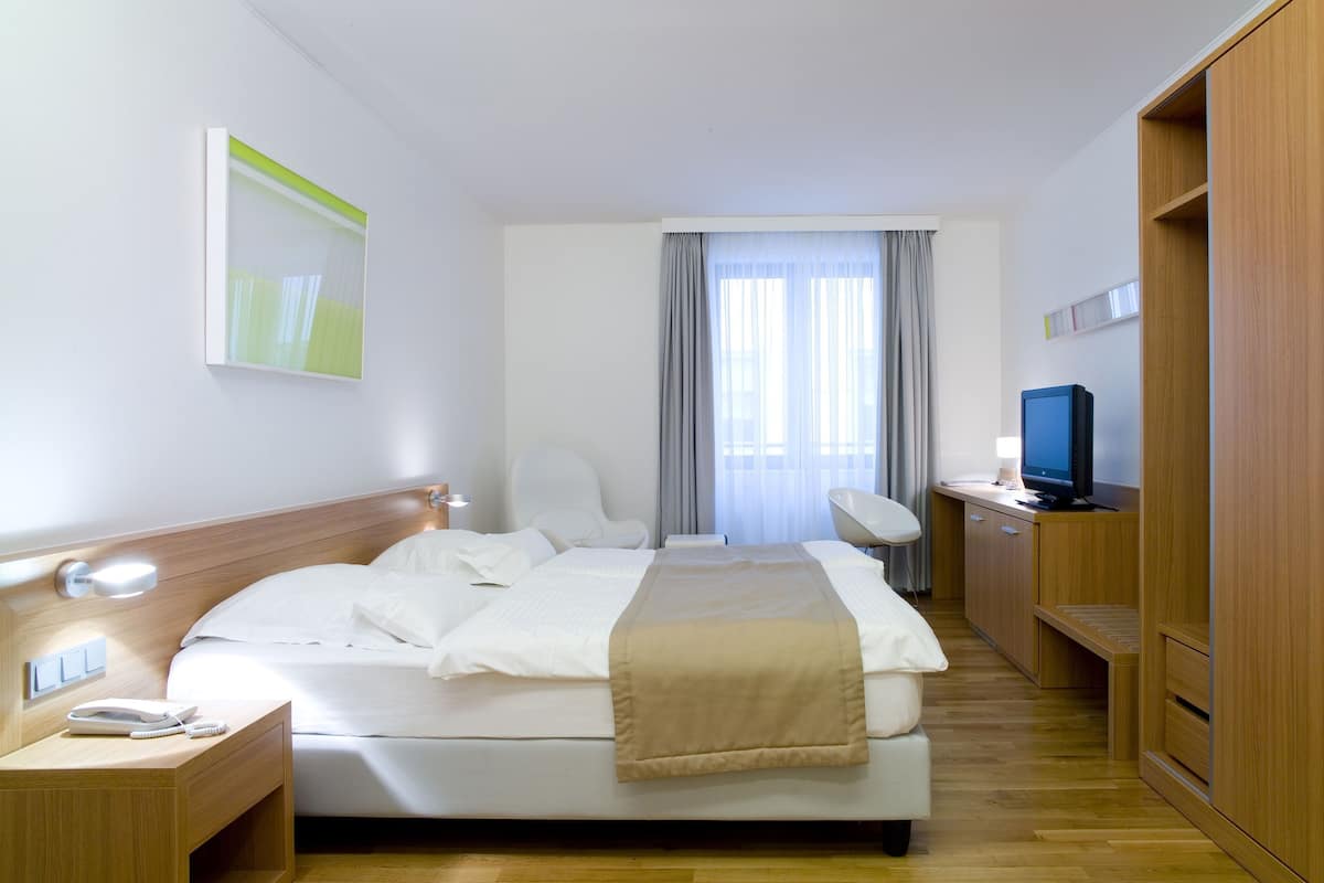 Une chambre d’hôtel comprenant un lit, une table de chevet, une lampe, une télévision et un bureau avec une chaise.