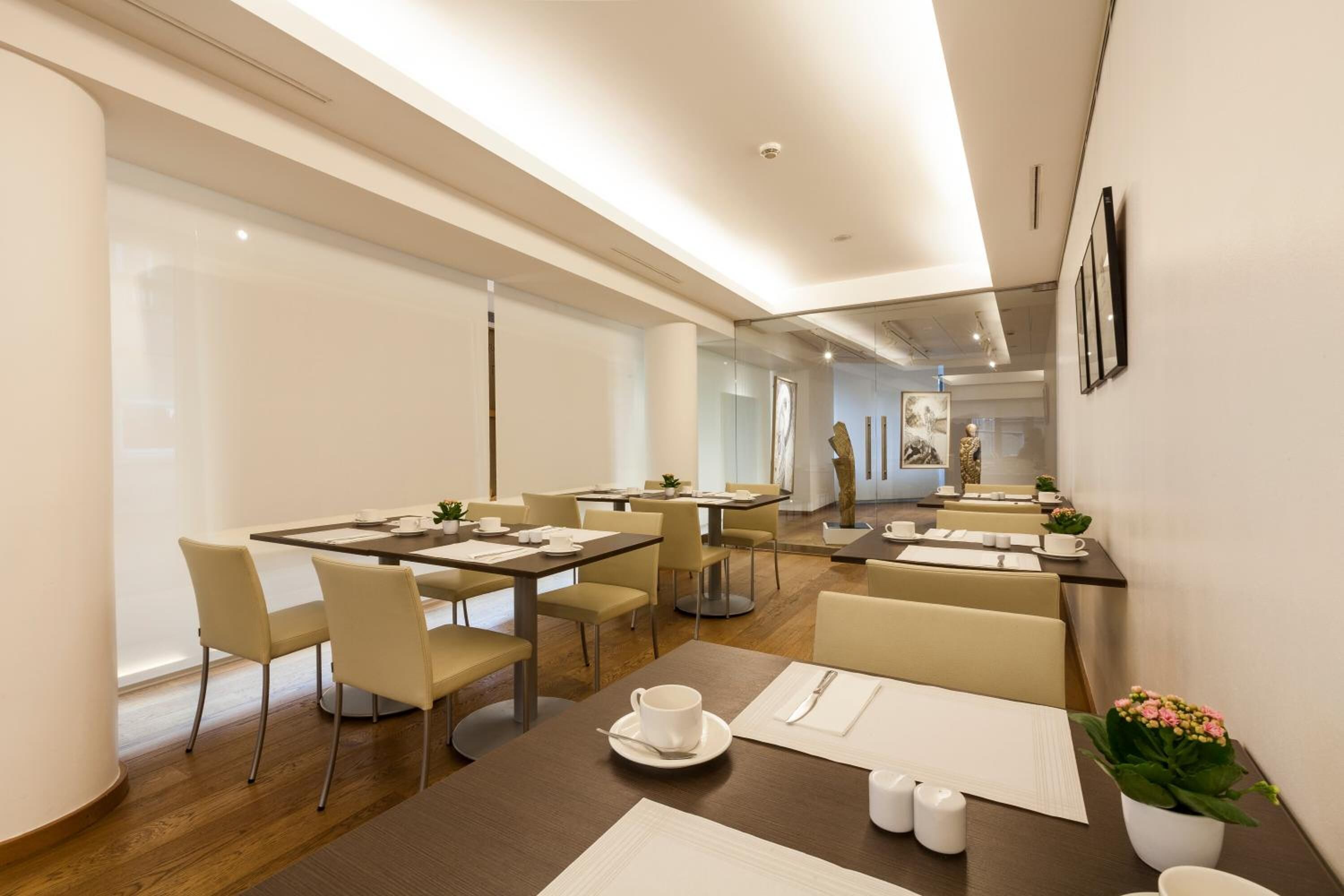 Un comedor moderno con varias mesas y sillas, suelo de madera y un amplio ventanal que proporciona luz natural.