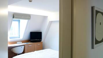 A bedroom with a bed, a desk with a computer, a chair, and a window.
