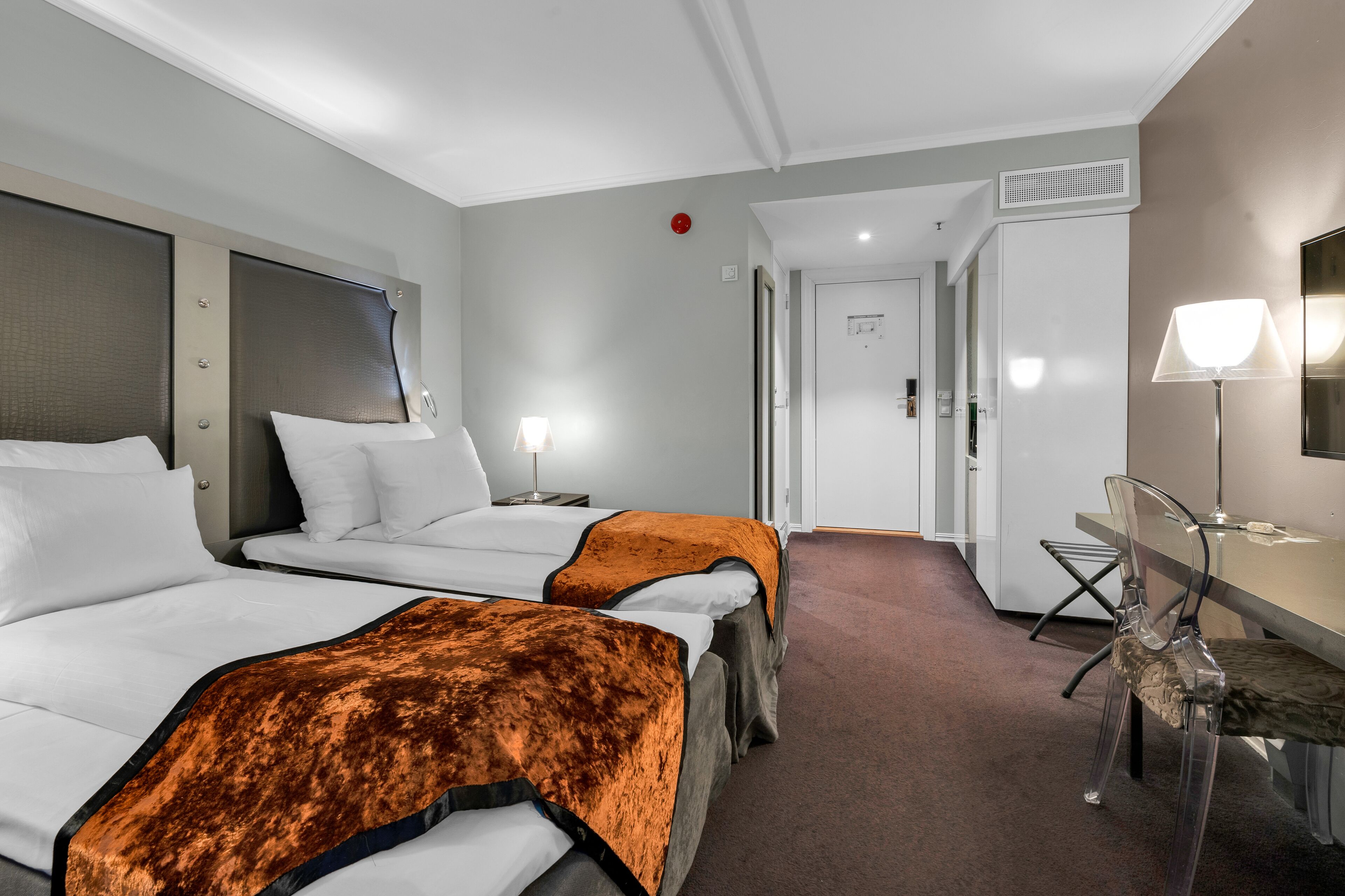 A hotel room with two beds, a desk, a chair, and a door leading to a bathroom.