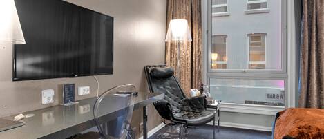 Une chambre d’hôtel équipée d’une télévision, d’un bureau avec une chaise, d’un lit et d’une fenêtre avec des rideaux.