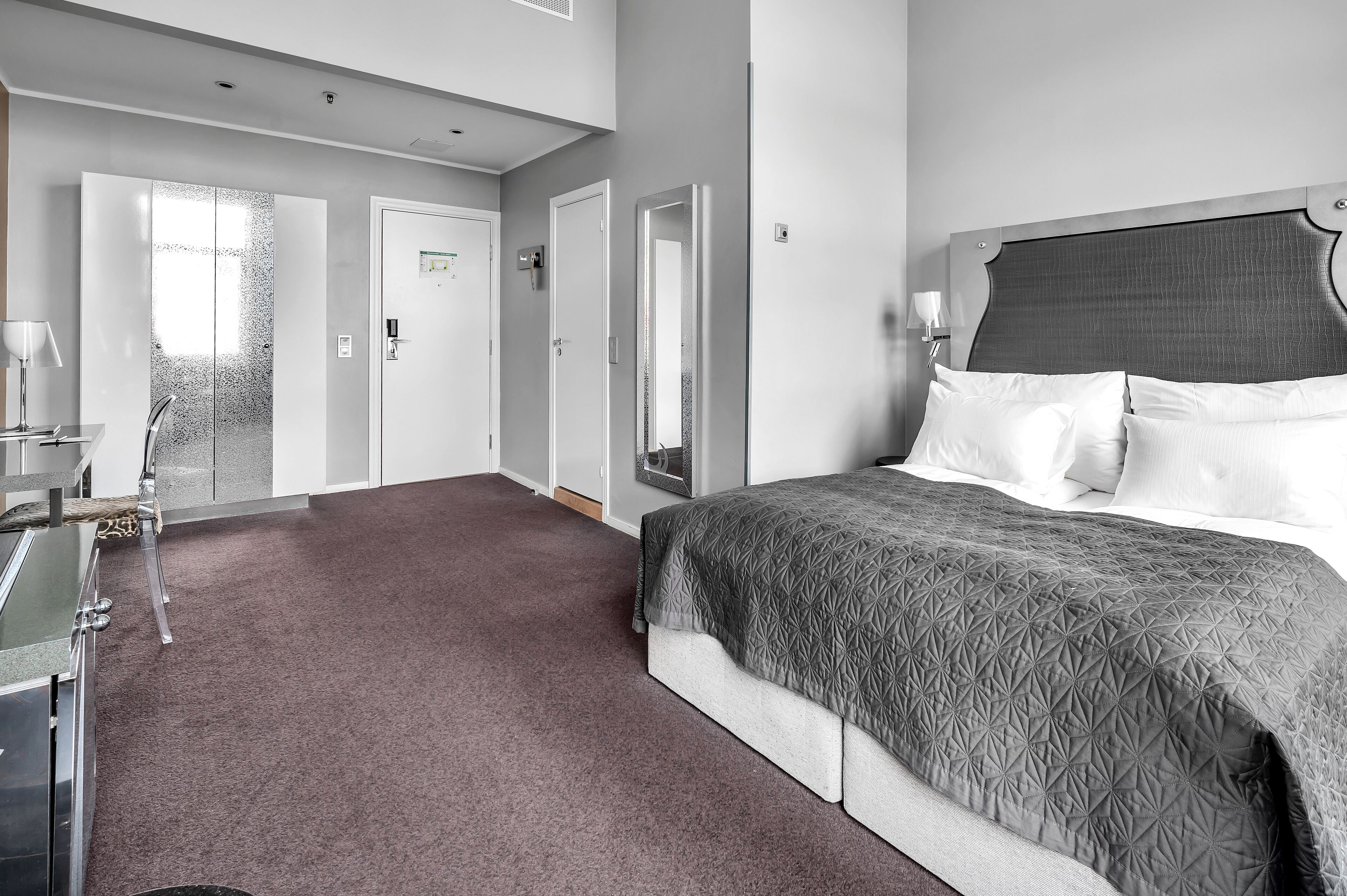 A modern hotel room with a large bed, a desk, and a mirror.