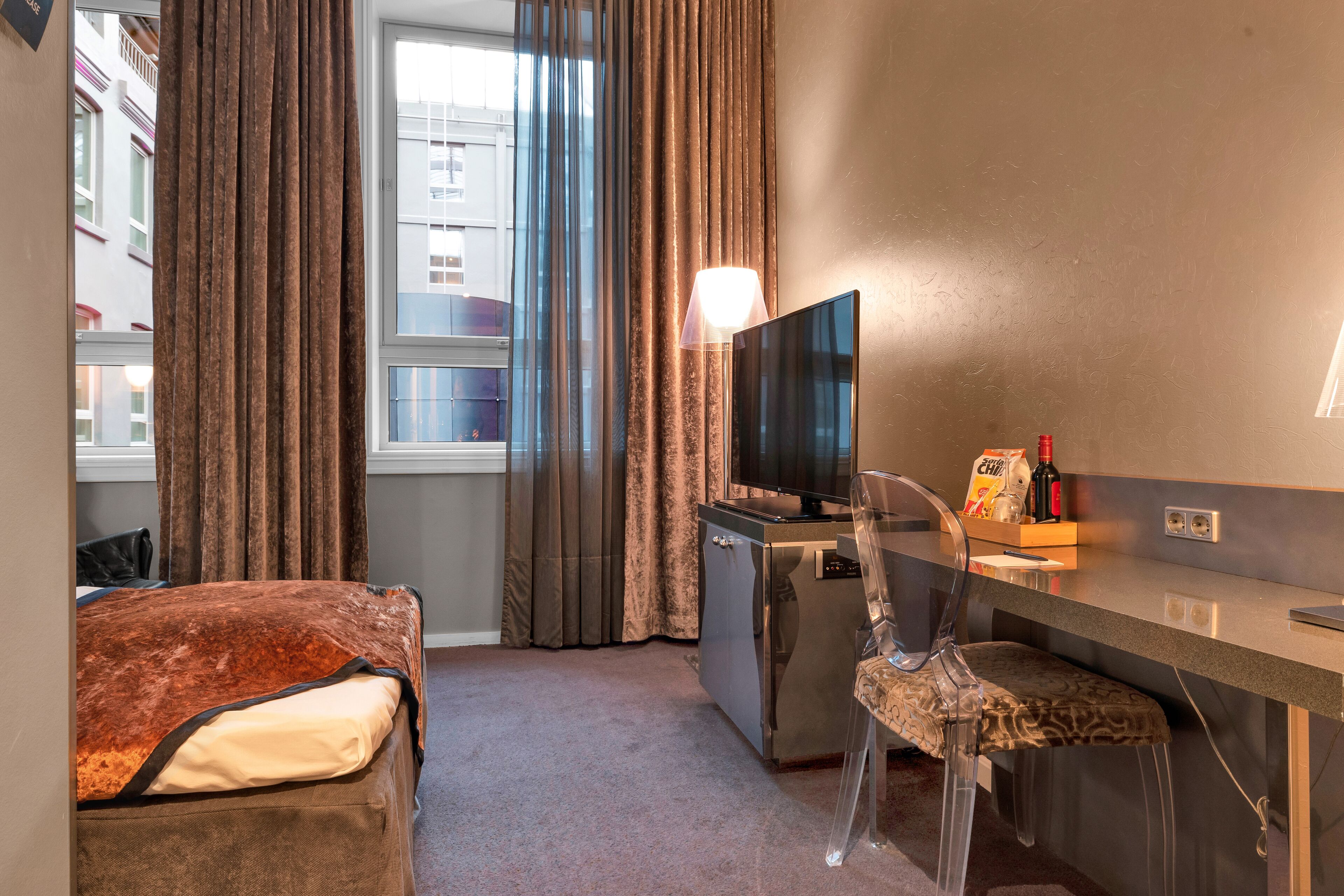 Ein Hotelzimmer mit Bett, Schreibtisch mit Fernseher, Stuhl und kleinem Kühlschrank.