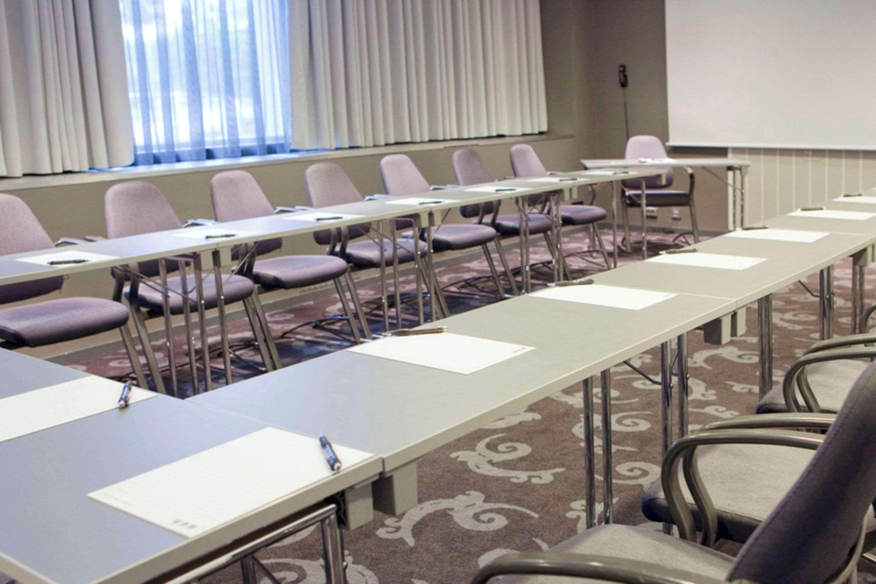 A conference room with a long table, chairs, and a projector screen.