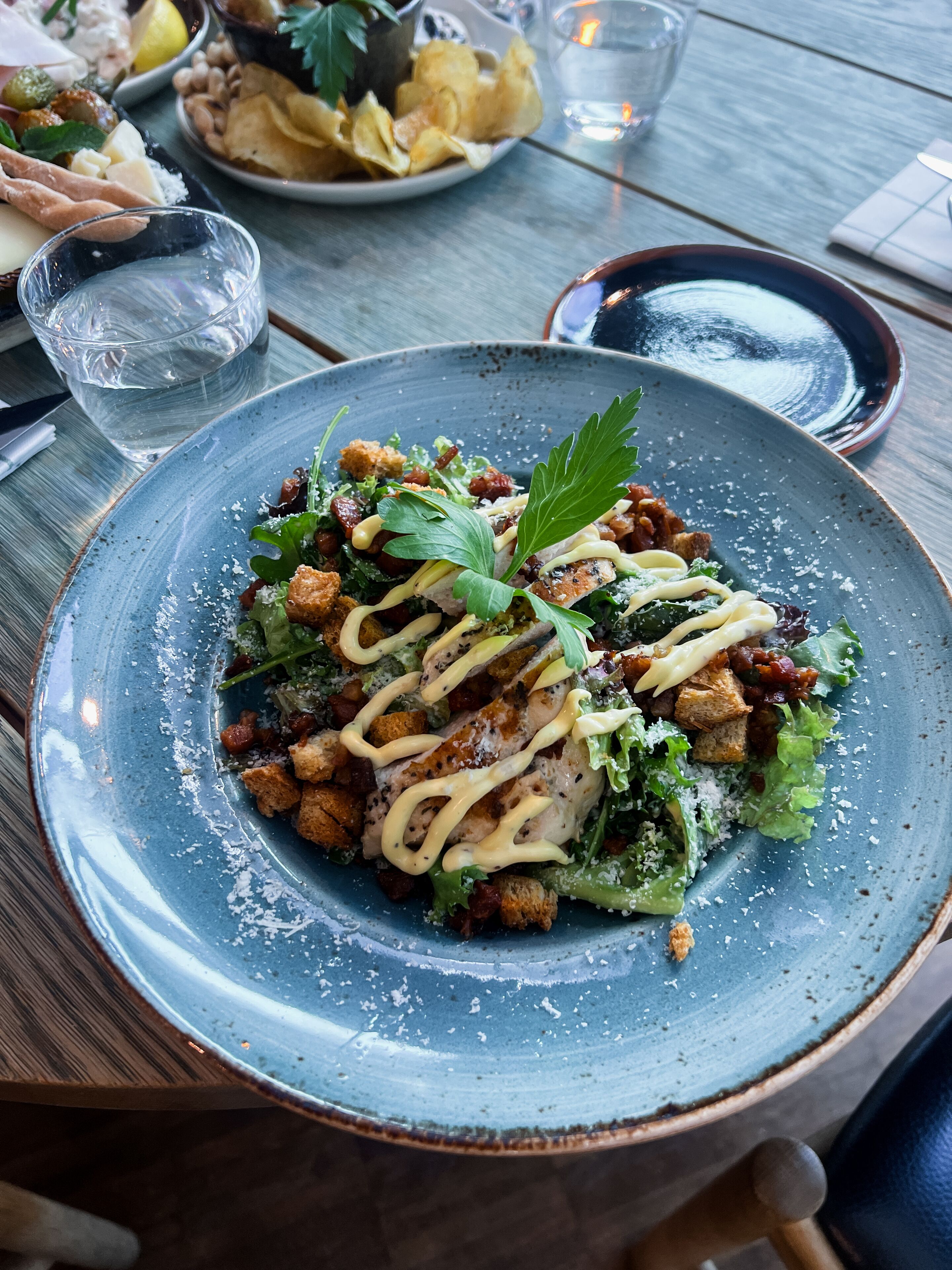 Ein blauer Keramikteller mit Salat, Croutons und einer Garnitur auf einem Holztisch.