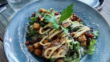 Ein blauer Keramikteller mit Salat, Croutons und einer Garnitur auf einem Holztisch.