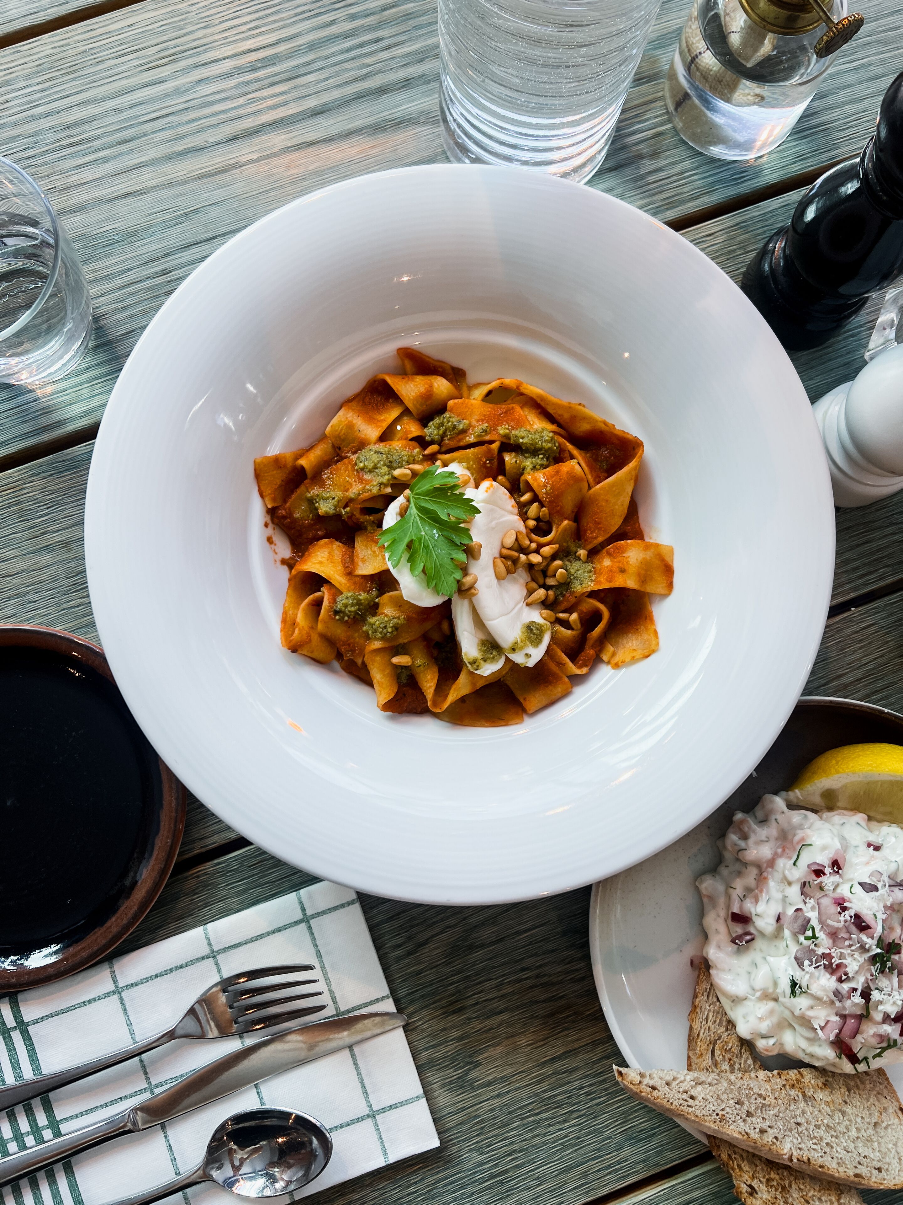Una mesa de comedor con un plato de pasta, un tazón de ensalada y un gajo de limón.