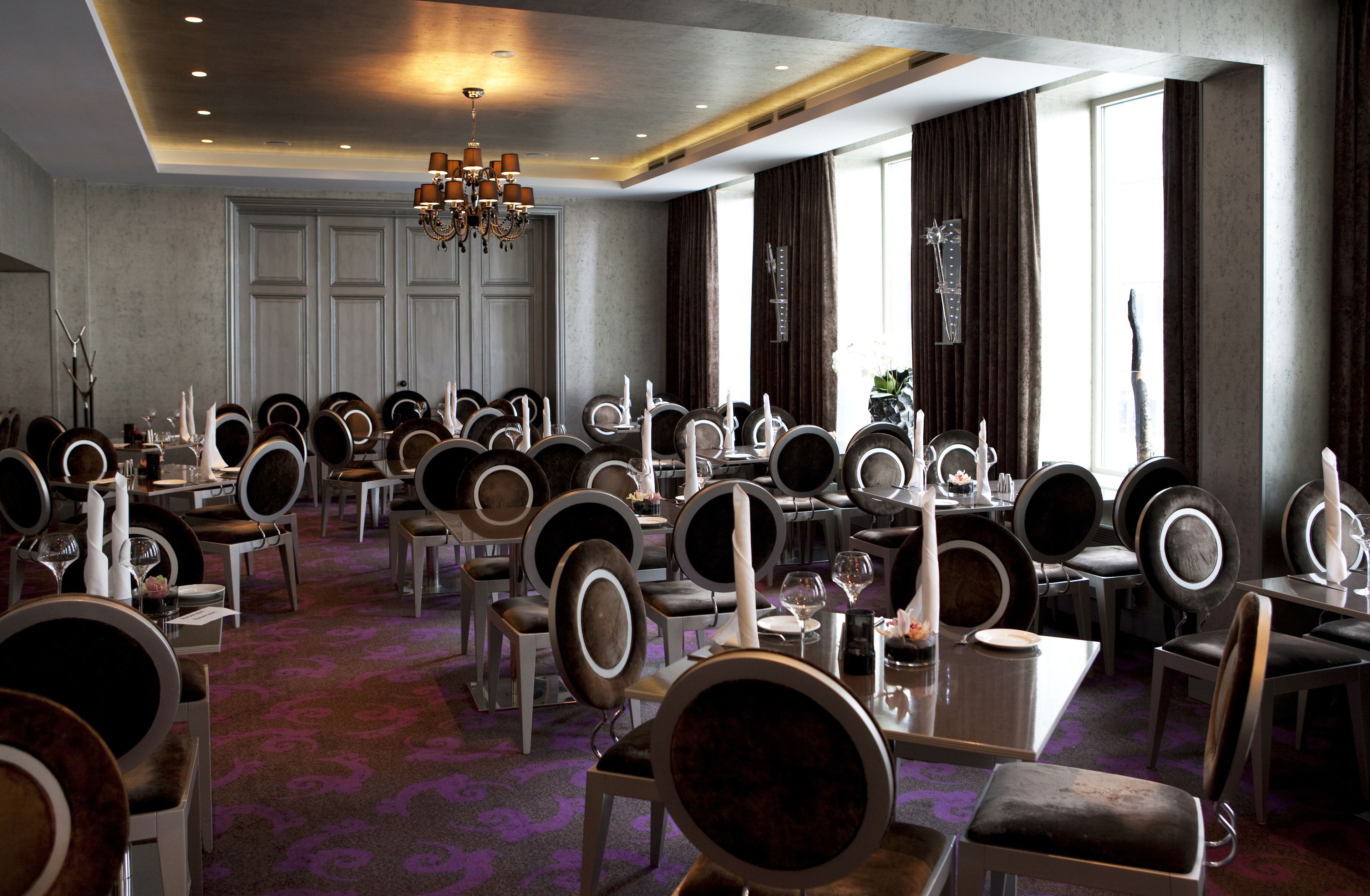 A conference room with multiple tables and chairs, a chandelier, and large windows with curtains.