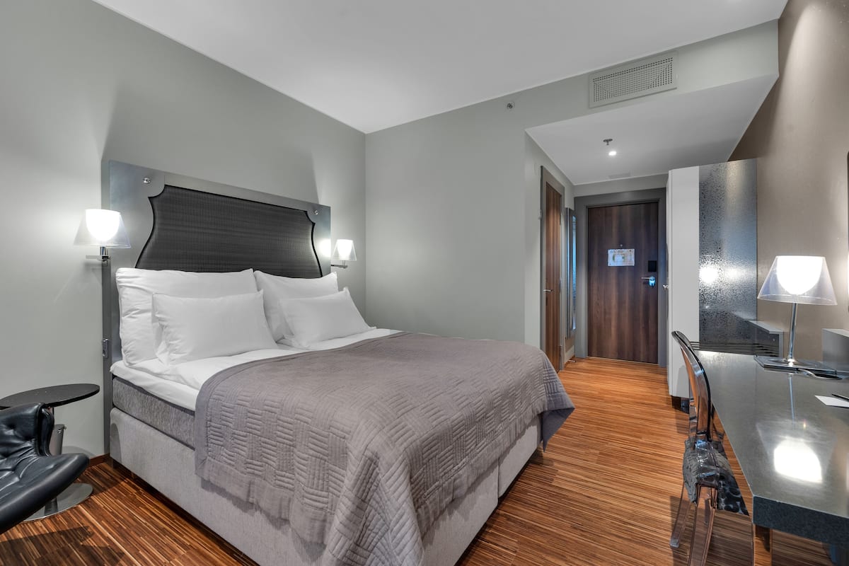 Ein modernes Hotelzimmer mit einem großen Bett, Nachttischlampen, einem Schreibtisch mit Stuhl und Holzboden.