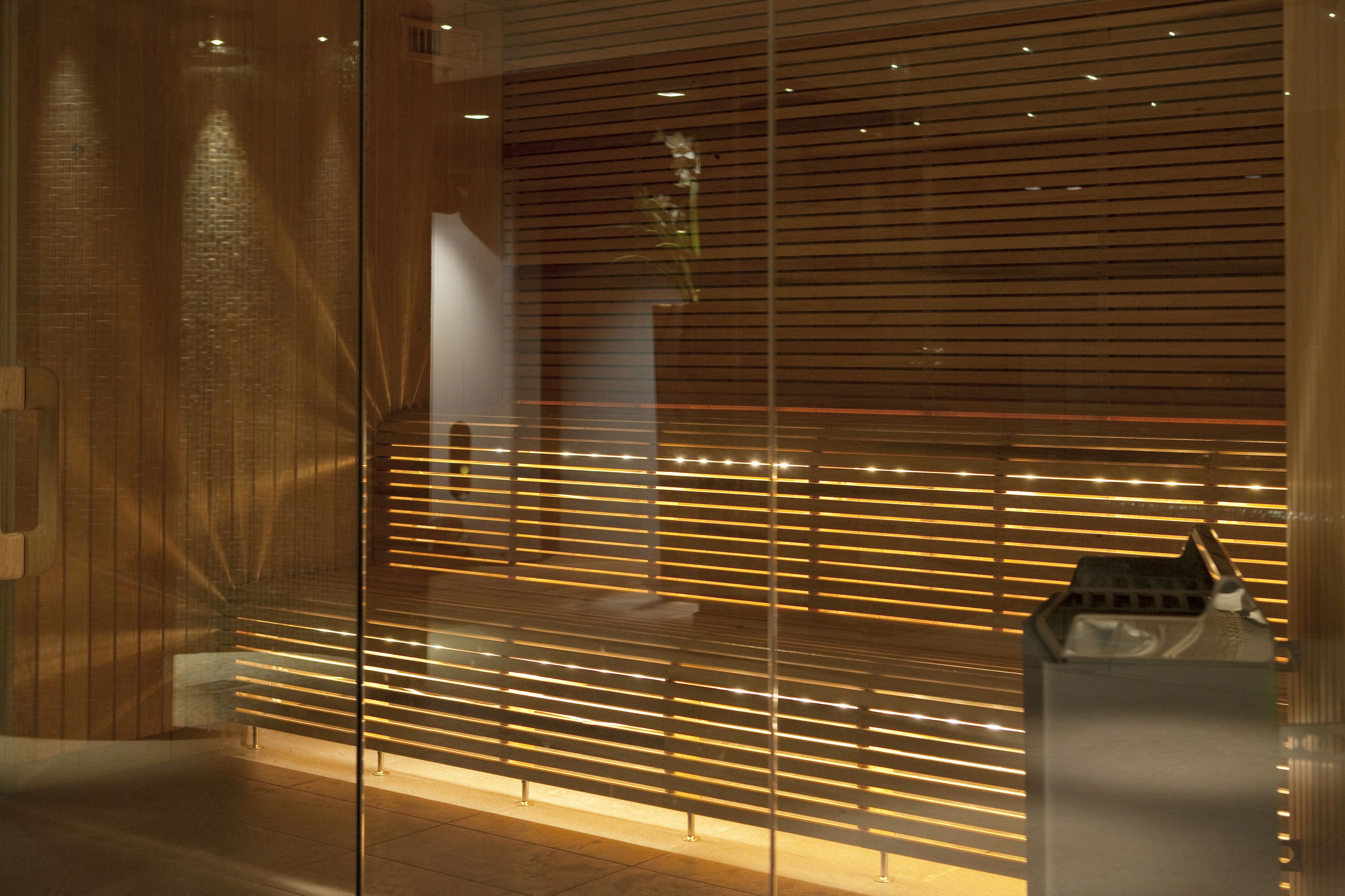 Un interior moderno con un separador de listones de madera, un banco y un pequeño objeto decorativo sobre un pedestal.