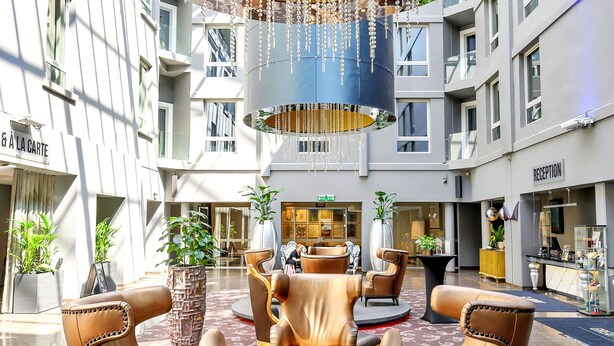 A spacious lobby with leather armchairs, a large chandelier, and a reception desk.