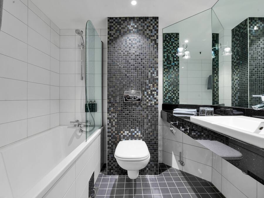 A modern bathroom with a bathtub, toilet, and a large mirror.