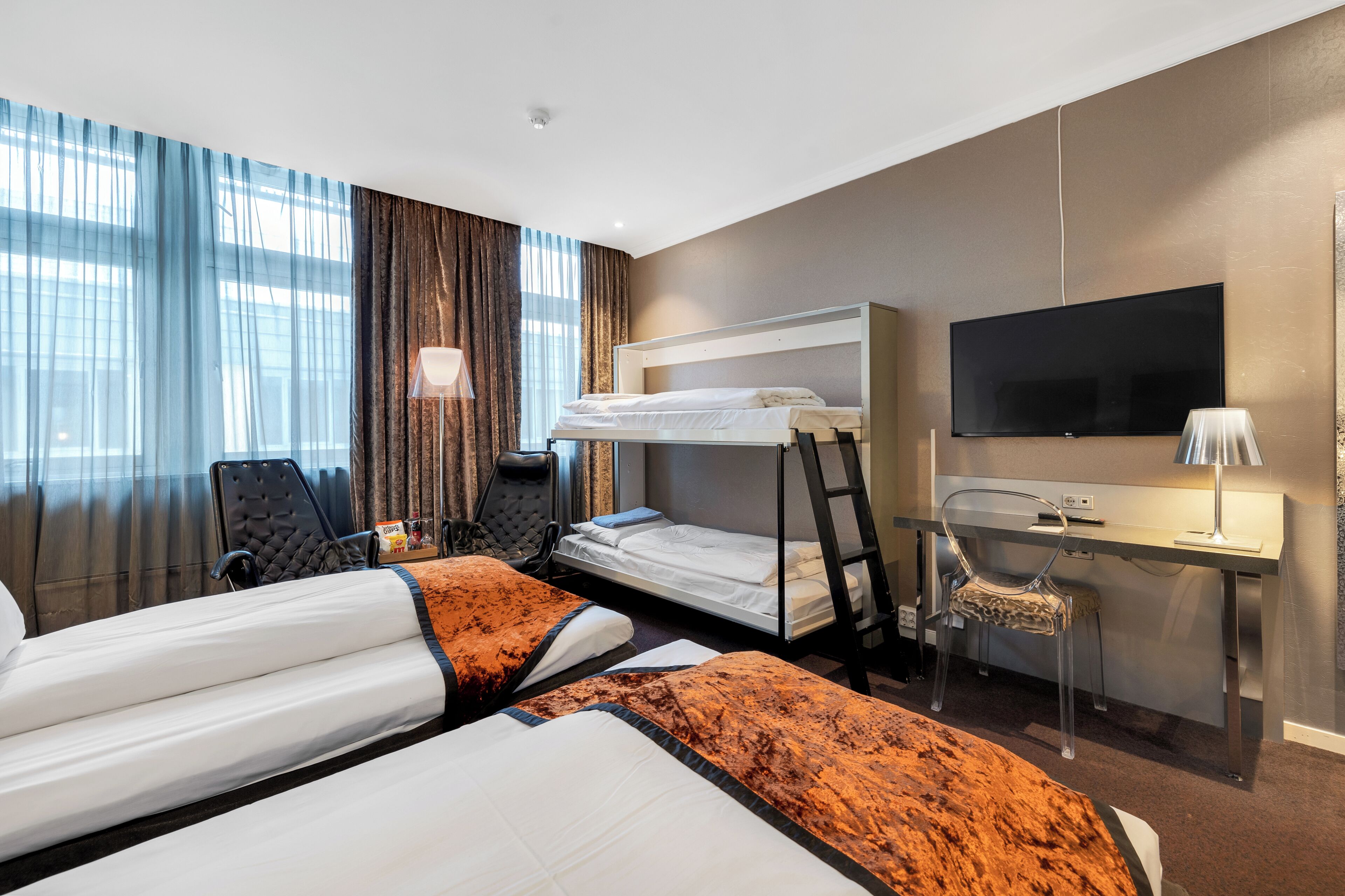A hotel room with two beds, a desk, a chair, a TV, and a window with curtains.