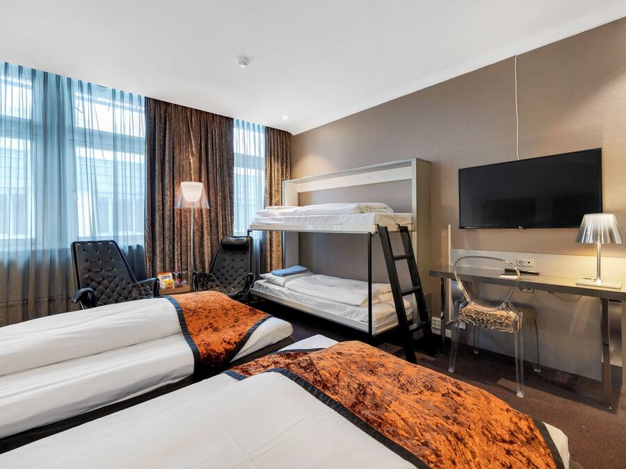 A hotel room with two beds, a desk, a chair, a TV, and a window with curtains.