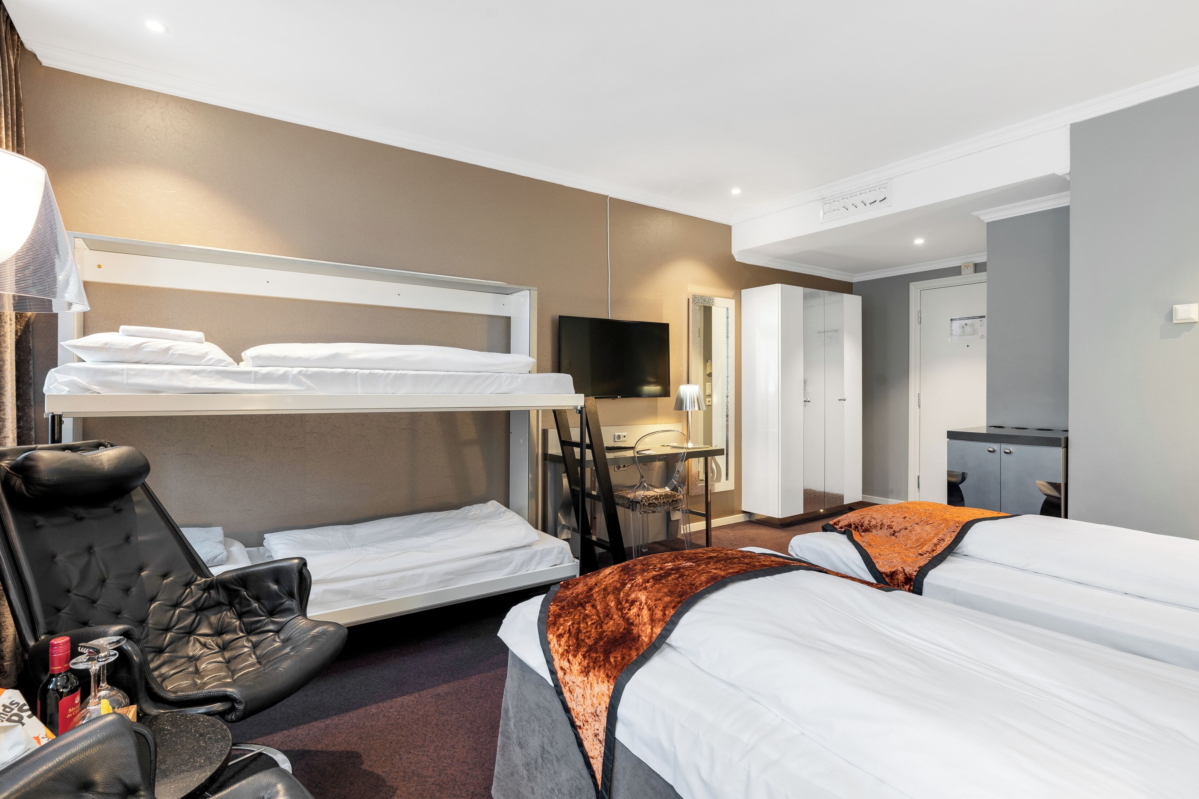Habitación de hotel con literas, un escritorio con silla, televisión y armario.