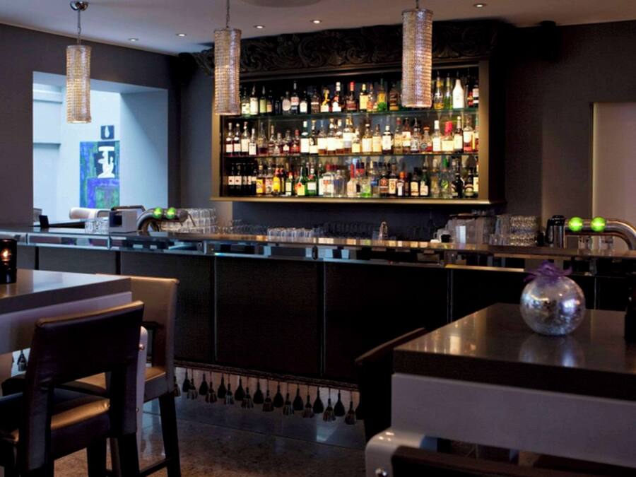 Zona de bar amb una estanteria ben repleta de licors, llums penjants i un mostrador modern.