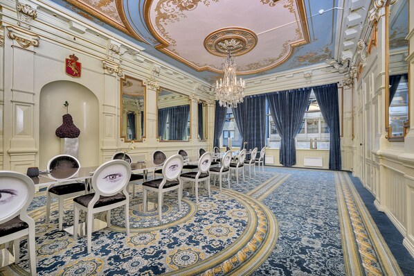 Un salón de reuniones formal con techo ornamentado, candelabros y alfombra estampada.