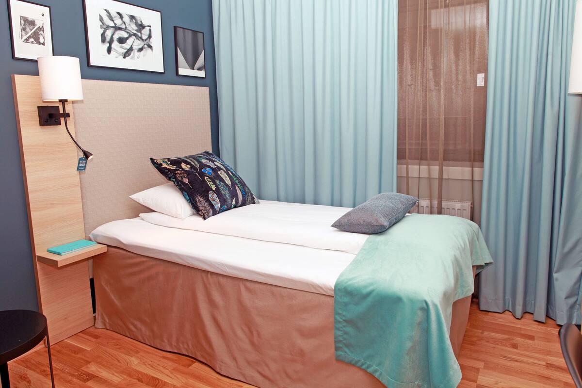 A bedroom with a bed, a nightstand, a chair, a window with curtains, and framed pictures on the wall.