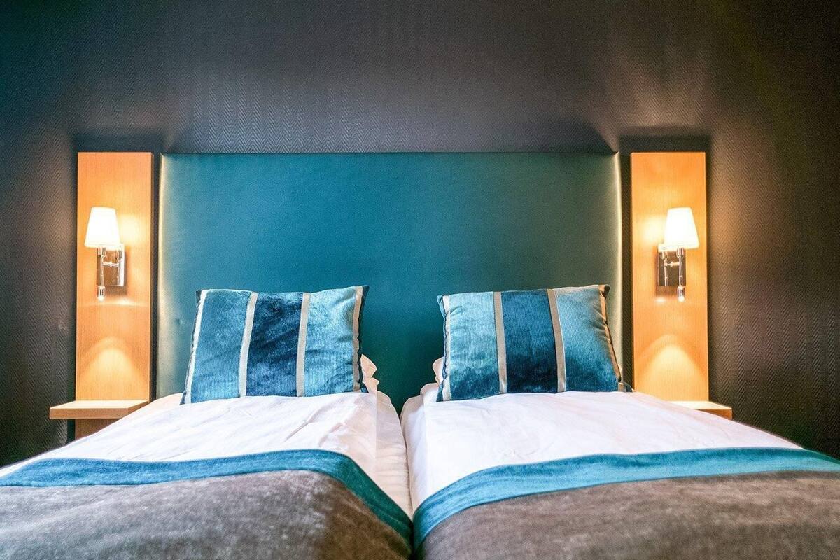 A double bed with two pillows and two bedside lamps against a dark wall.