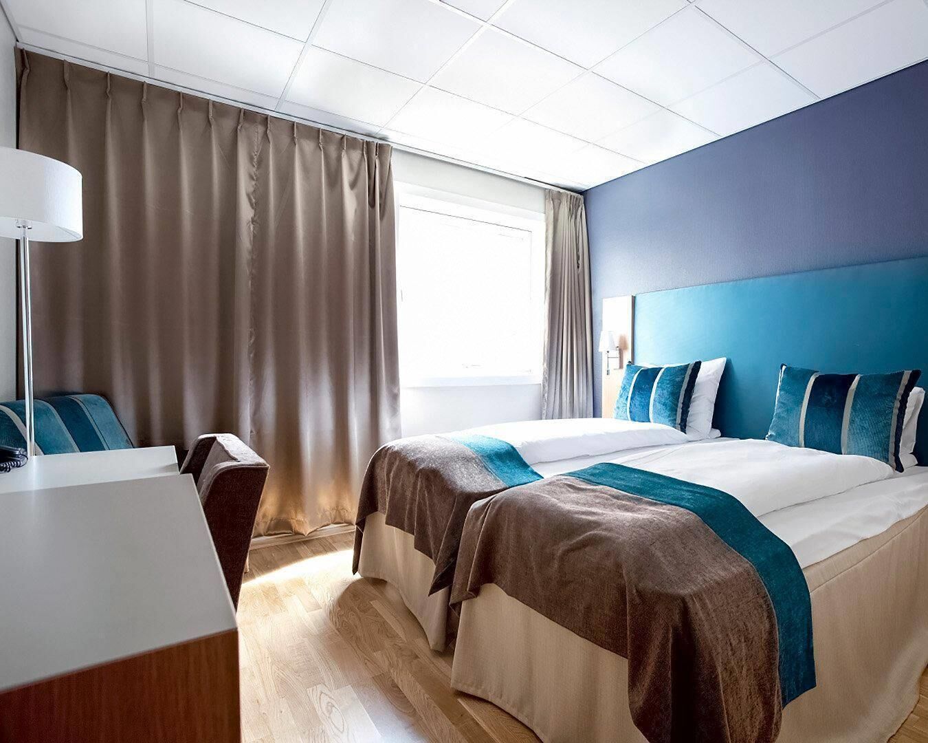 Habitación de hotel con dos camas, un escritorio y una ventana con cortinas.