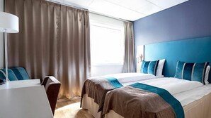 Habitación de hotel con dos camas, un escritorio y una ventana con cortinas.