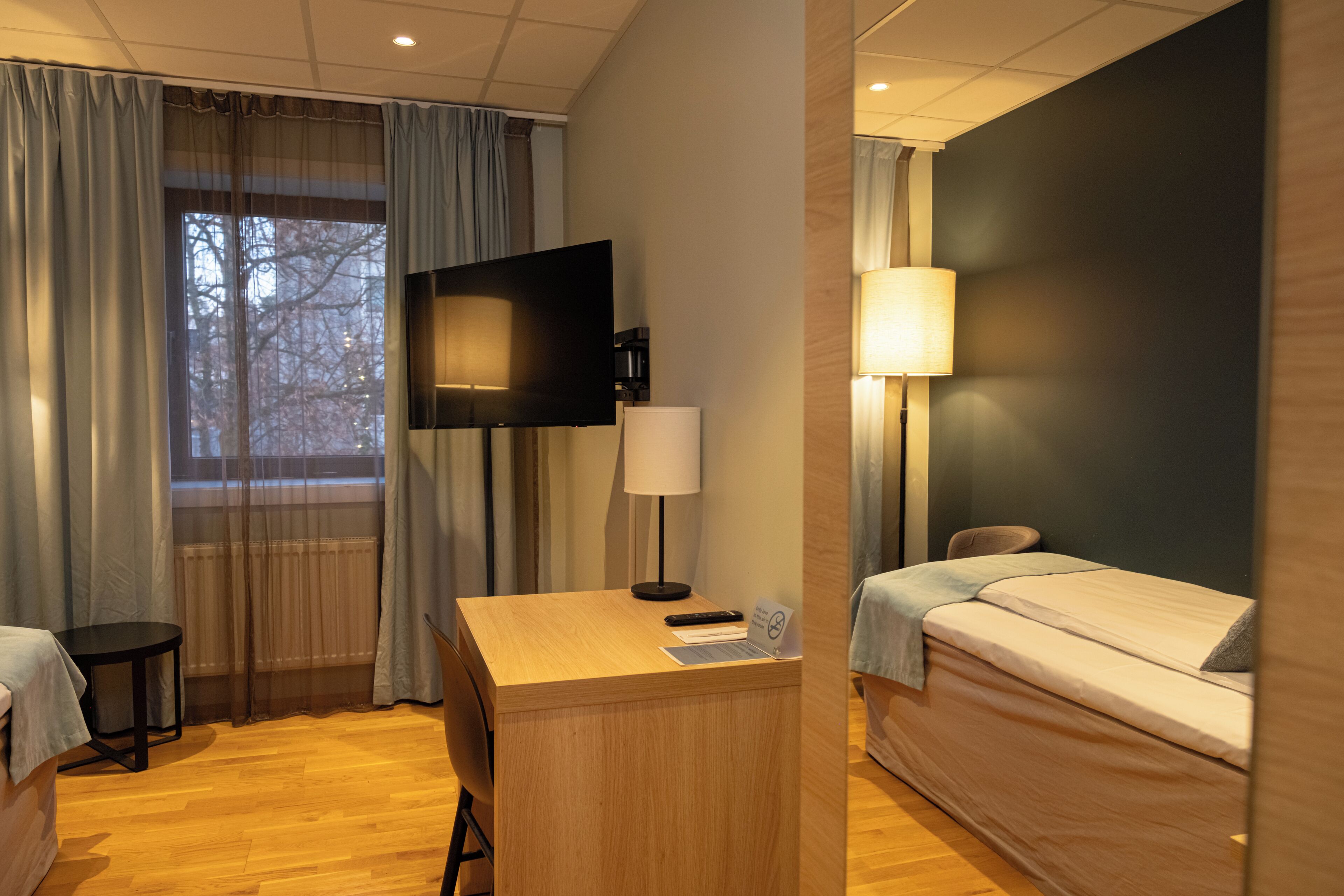 Una habitación de hotel con cama, escritorio, televisión y lámpara.