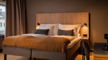 Une chambre moderne avec une tête de lit en bois, deux tables de chevet avec des lampes, un lit recouvert d’une couverture marron et un bureau avec une chaise.
