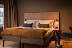 A modern bedroom with a wooden headboard, two bedside tables with lamps, a bed with a brown blanket, and a desk with a chair.