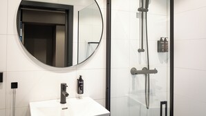 Un baño moderno con un espejo redondo, un lavamanos blanco y una zona de ducha con paredes de vidrio.