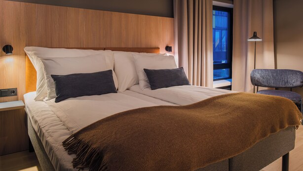 Una cama bien hecha con una manta marrón, un cabecero de madera y una mesita de noche con una lámpara.
