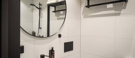 A modern bathroom with a round mirror, a black towel rack, a white sink, and a toilet paper holder.